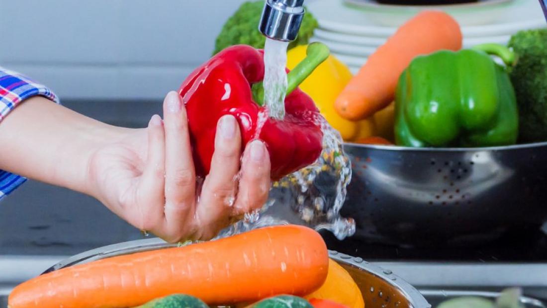 personne lavant des légumes sous un jet d'eau du robinet de cuisine