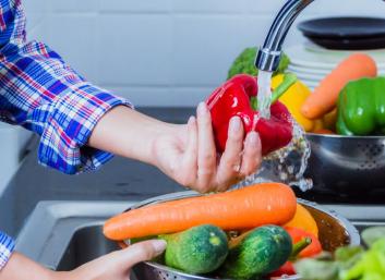 personne lavant des légumes sous un jet d'eau du robinet de cuisine